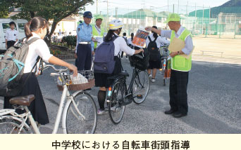 中学校における自転車街頭指導。自転車を押す学生に指導する警察官と自治会会員の写真