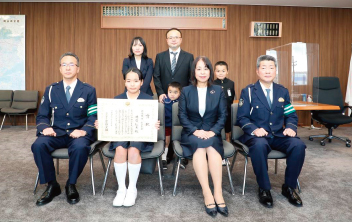 小学生の部 最優秀作 受賞者。表彰状を手に持つ明石さんと関係者の写真